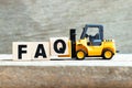 Toy forklift hold block q to complete word FAQ Abbreviation of Frequently Asked Questions on wood background