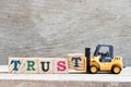 Toy forklift hold letter block t to word trust on wood background