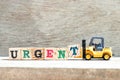 Toy forklift hold letter block t to complete word urgent on wood background