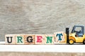 Toy forklift hold block t to complete word urgent on wood background