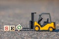 A toy forklift lifts a block with the letter O to complete the word SEO search engine optimization abbreviation from the