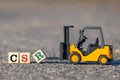 A toy forklift lifts a block with the letter R in CSR abbreviation for corporate social responsibility from the asphalt