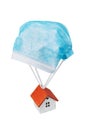 Toy house flies on a parachute from a medical mask isolated on a white background. Concept on a safe place during a pandemic Royalty Free Stock Photo