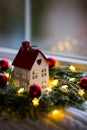 Toy house with hole in form of heart near fir wreath decorated with red Christmas balls and coiled with glowing garland with warm Royalty Free Stock Photo