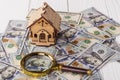 A toy house made of wood with a roof costs money, on a hundred-dollar bill, next to a magnifying glass. Concept: mortgage, Royalty Free Stock Photo