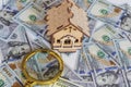 A toy house made of wood with a roof costs money, on a hundred-dollar bill, next to a magnifying glass. Concept: mortgage, Royalty Free Stock Photo