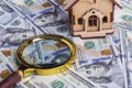 A toy house made of wood with a roof costs money, on a hundred-dollar bill, next to a magnifying glass. Concept: mortgage, Royalty Free Stock Photo