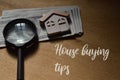 Toy house, money and magnifying glass over wooden background written with HOUSE BUYING TIPS Royalty Free Stock Photo