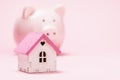 Toy house and piggy bank on a pink background with copy space. Concept of accumulating money to buy a house