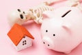 Toy house, piggy bank and skeleton on a pink background. The concept of accumulating money to buy a house until death Royalty Free Stock Photo
