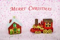 Toy houses a train of red golden flowers on a pink confetti background with the inscription Merry Christmas Royalty Free Stock Photo