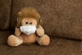 toy lion sits on a sofa in a medical mask.