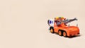 Toy orange tow truck on beige background banner with space for text. Children`s car for loading and transporting cars