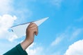 Toy paper airplane in child hand against cheerful blue sky with white clouds. Children dreams, inspirations and the future concept