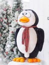 A toy penguin standing against Christmas trees surrounded with gift boxes.