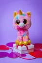 Toy Pink Unicorn sits on a white gift box with a Red Ribbon on paper hearts on a purple background Royalty Free Stock Photo