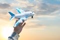 Toy plastic airplane in hand against blue sky and sunset. Dreams, vacation or travel concept. Vintage toned effect.