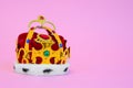 Toy plastic royal crown decorated with fake gems, fur and red cloth on pink background, studio shooting, front view Royalty Free Stock Photo