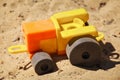 A toy plastic tractor on the sand of a playground.