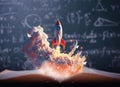 Toy rocket takes spewing smoke on a book in green blackboard background. The symbol for success is Start-up education and