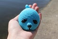 A toy seal in the hands of a young unrecognizable girl on the background of the lake. Blue seal in nature. Knitted