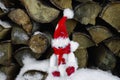 A toy snowman with a red hat sits in the snow near a pile of firewood Royalty Free Stock Photo