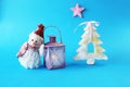 Toy snowman in a Santa hat, lantern with a lit candle on a blue bright background, Merry Christmas concep Royalty Free Stock Photo