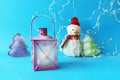 Toy snowman in a Santa hat, lantern with a lit candle on a blue bright background Royalty Free Stock Photo