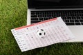 Toy soccer ball and betting list near laptop on green grass