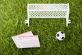 Toy soccer ball near miniature football gates and betting lists on green grass