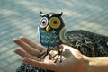 A toy of a surprised blue owl with multi-colored eyes close-up stands on the palm of a female hand in the light of the evening sun