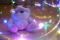 A toy teddy bear surrounded by colored lights. Abstract fairytale magic background