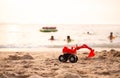 Toy tractor on sand beach at coast with child playing on sea blured