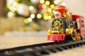 Toy train and railway on floor against Christmas lights. Space for text Royalty Free Stock Photo