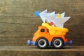 Toy truck carrying hand made paper christmas tree against rough wooden background. Side view. Christmas tree recycle or disposal, Royalty Free Stock Photo