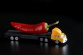 Toy truck carrying a large red chili pepper. Black background. The concept of delivering oversized items and fresh vegetables from Royalty Free Stock Photo