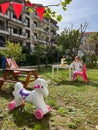 Toy unicorn stands in the yard near a little girl sitting at the table