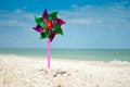 Toy windmill close-up on the background of sand of the sea and sky, children`s game toy colored blades pinwheel weather vane