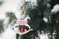 Toy winter horse with ornament hanging on spruce branch covered with snow. Royalty Free Stock Photo