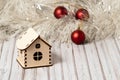 Toy wooden house on a wooden table decorated with a garland and red Christmas balls for New Year or XMAS