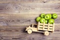 Toy wooden truck with green apples in the back on wooden backgr