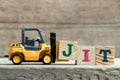 Toy yellow forklift hold letter block J to complete word JIT Abbreviation of Just in time