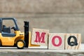 Toy yellow forklift hold letter block M to complete word MOQ (Abbreviation of Minimum Order Quantity)on wood background