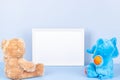 Toys with empty white frame on light blue background. Toy teddy bear, plush stuffed elephant and white wooden picture Royalty Free Stock Photo