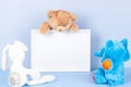 Toys with empty white frame on light blue background. Toy teddy bear and plush stuffed toys and white wooden picture Royalty Free Stock Photo