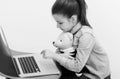 Adorable girl hugging cute teddy bear and typing on laptop Royalty Free Stock Photo