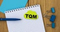 TQM - word written in a notebook on a wooden background with a pen and clamps Royalty Free Stock Photo