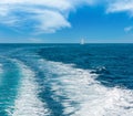 Trace tail of speed boat or ferry on water surface in the sea and white sailing vessel in far. Natural and vacation background Royalty Free Stock Photo