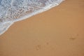 Traces of bare human feet on the sand. Sea waves with white foam run over thesand Royalty Free Stock Photo