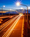 Traces of headlights from cars moving at night on the bridge, illuminated by lanterns. Abstract cityscape with highway at dusk Royalty Free Stock Photo